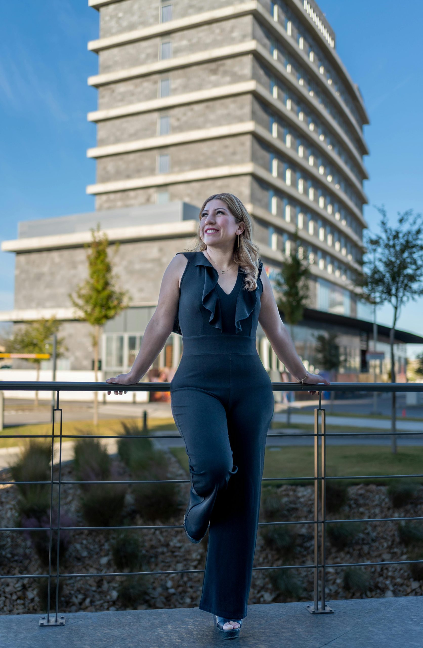 Stylish woman in a jumpsuit poses confidently in Juárez's modern urban setting.