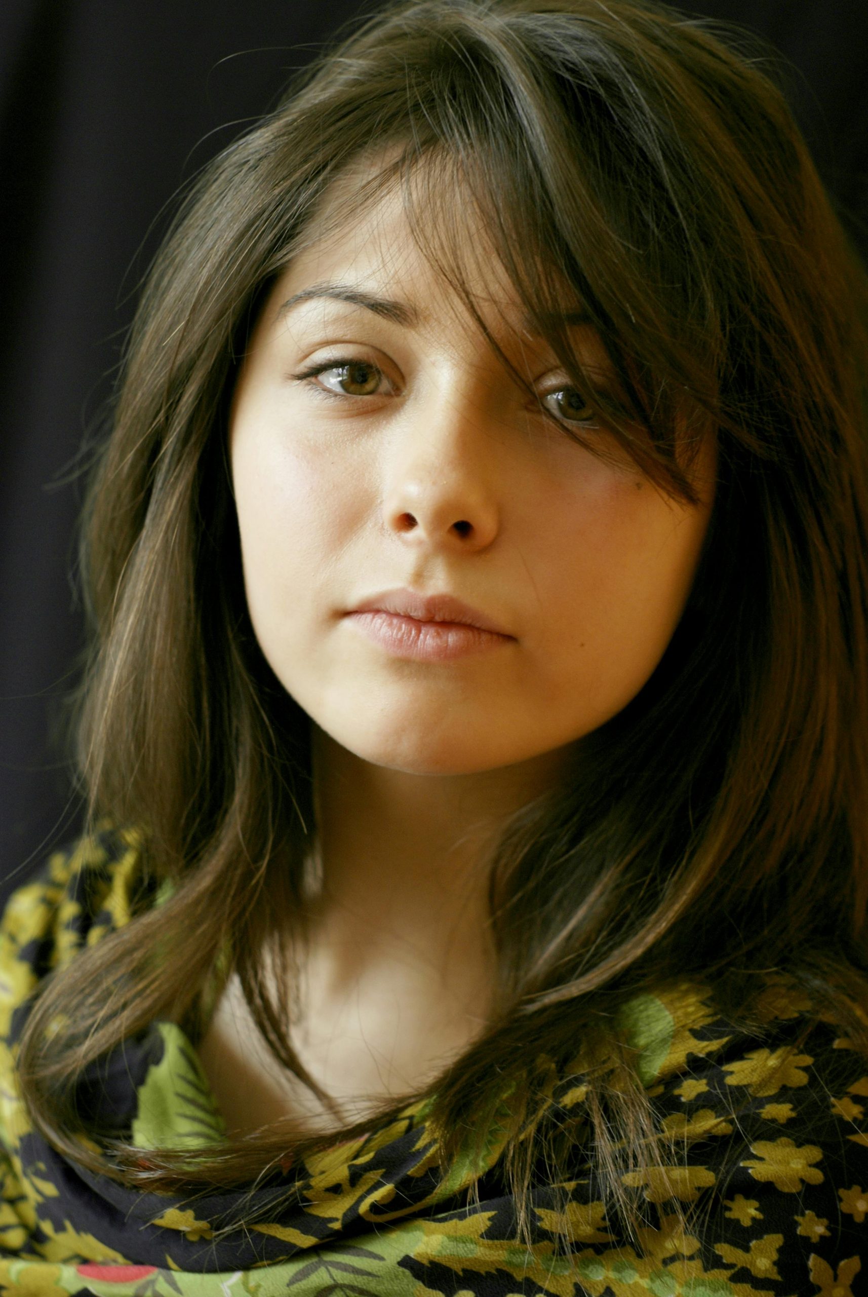 Elegant portrait of a young woman with long brunette hair in a floral top.